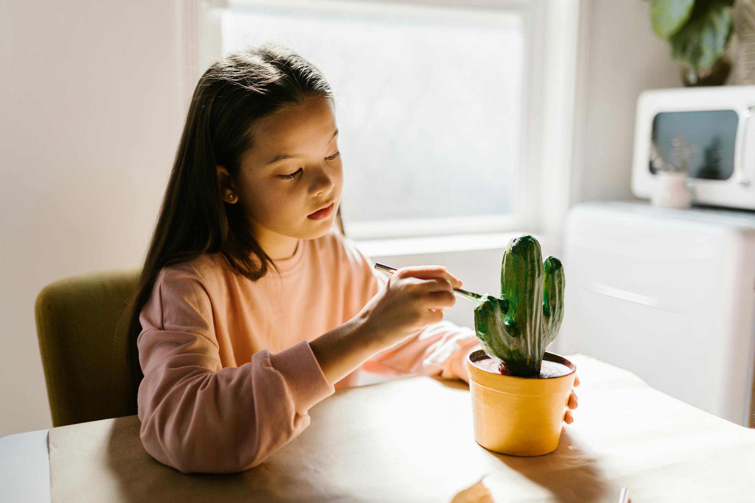 A young girl painting a cactus model indoors, engaged in mindful art