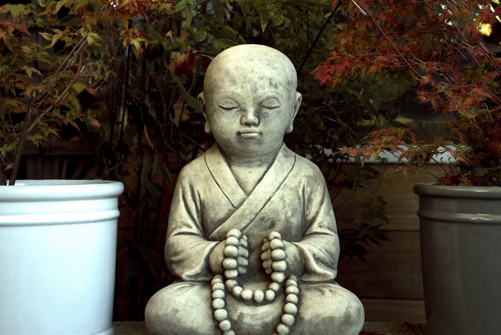 Zen Buddhist statue in tranquil garden with autumn leaves.