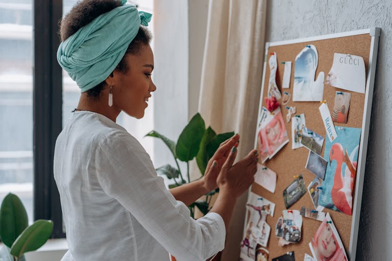 A woman arranging a creative vision board with diverse images and notes in a stylish interior.