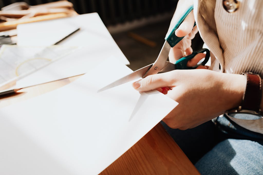 Art Prompts for cutting paper with scissors on a wooden table in a sunlit studio.